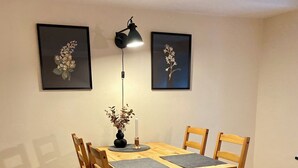 A dining area with a wooden table and chairs, two framed floral paintings on the wall, a floor lamp, and a candle on the table. - 1.5-room apartment with terrace (Pirna)