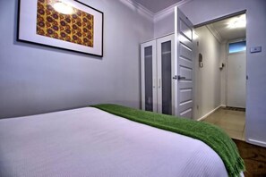 A bedroom with a bed, a green throw, a framed picture, and a closet with sliding doors.