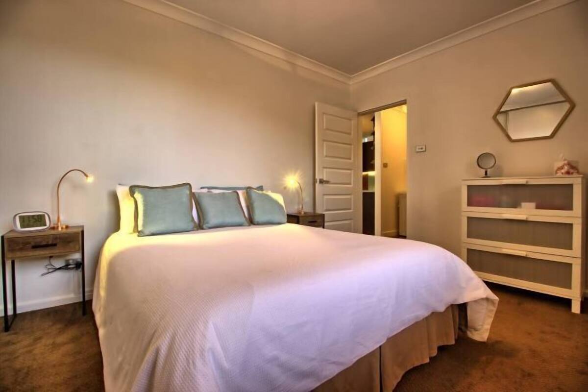 Een netjes ingerichte slaapkamer met een groot bed, nachtkastjes, een dressoir en een spiegel aan de muur.