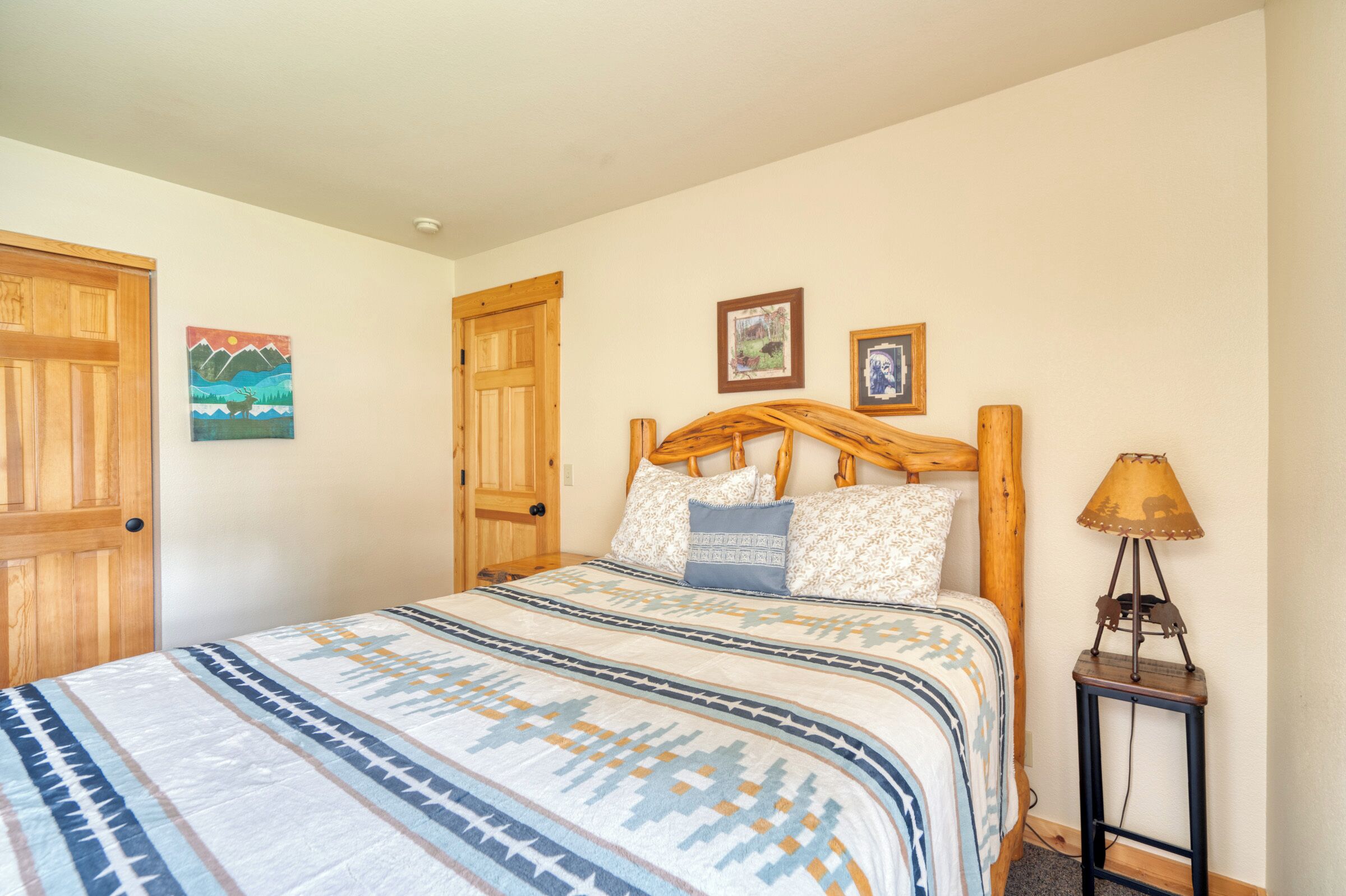 Une chambre à coucher avec un lit, une tête de lit en bois, deux tableaux encadrés, une lampe et une porte.