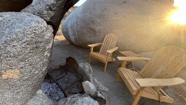 A beach setting with large rocks, wooden chairs, and a metal grill. - A Cozy Sunrise Glamping Escape with Panoramic View (Fallbrook)