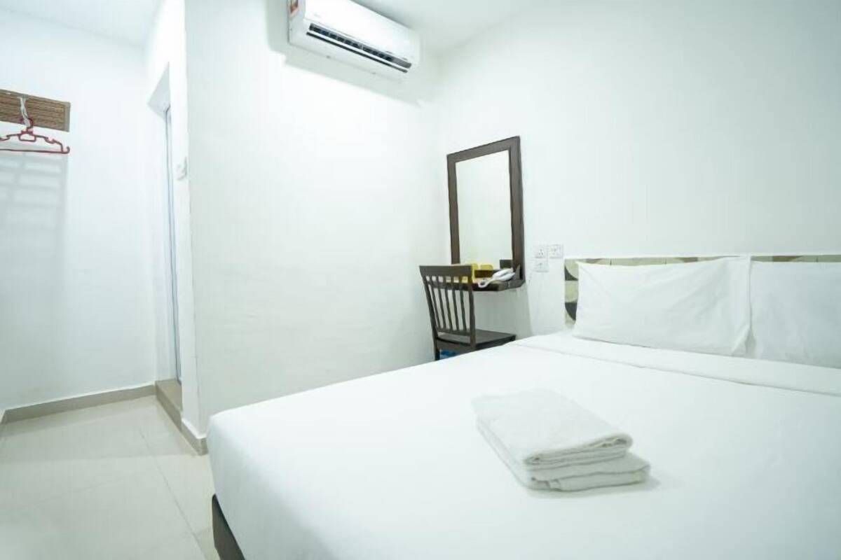 A hotel room with a bed, a chair, a mirror, and an air conditioning unit.