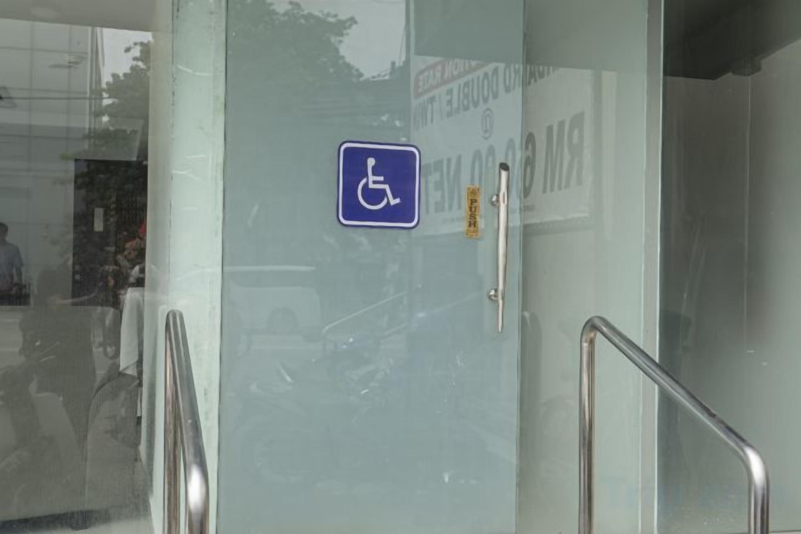 A door with a wheelchair accessibility sign, a metal handrail, and a door handle.