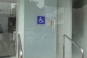 A door with a wheelchair accessibility sign, a metal handrail, and a door handle. - Grand Bagan Hotel (Butterworth)