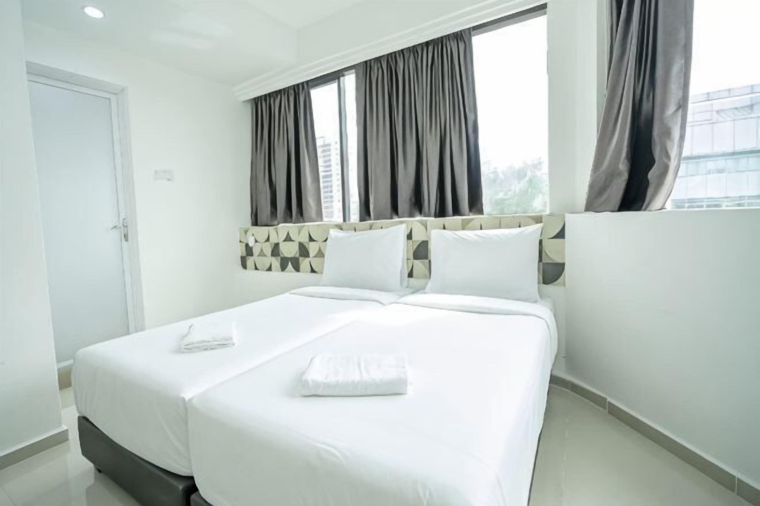 A hotel room with a large bed, a headboard with a geometric pattern, and a window with curtains.