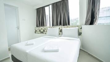 A hotel room with a large bed, a headboard with a geometric pattern, and a window with curtains.