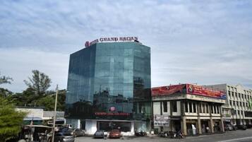A modern hotel with a glass facade, a prominent sign, and a street view with parked cars and a clear sky.