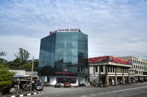 A modern hotel with a glass facade, a prominent sign, and a street view with parked cars and a clear sky.