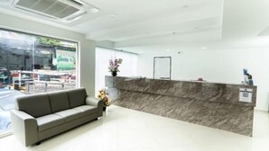 A modern reception area with a marble counter, a grey sofa, and a vase of flowers. - Grand Bagan Hotel (Butterworth)