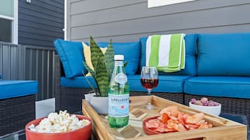 Ein Holztablett mit Popcorn, Chips, einer Flasche Sprudelwasser und einem Glas Rotwein auf einem Tisch vor einer blauen Couch mit einem grün-weißen Streifenhandtuch.