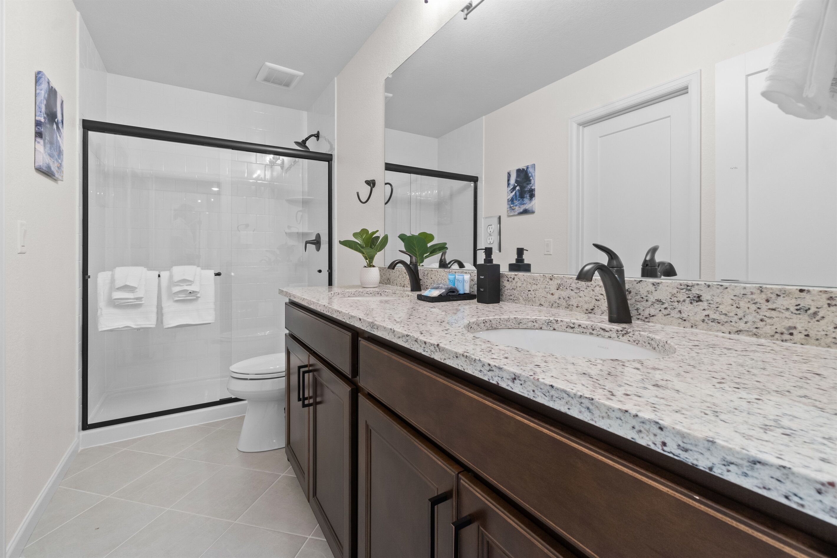 A modern bathroom with a glass shower enclosure, a large mirror, a granite countertop, and a toilet.