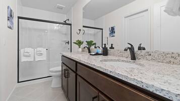 A modern bathroom with a glass shower enclosure, a large mirror, a granite countertop, and a toilet.