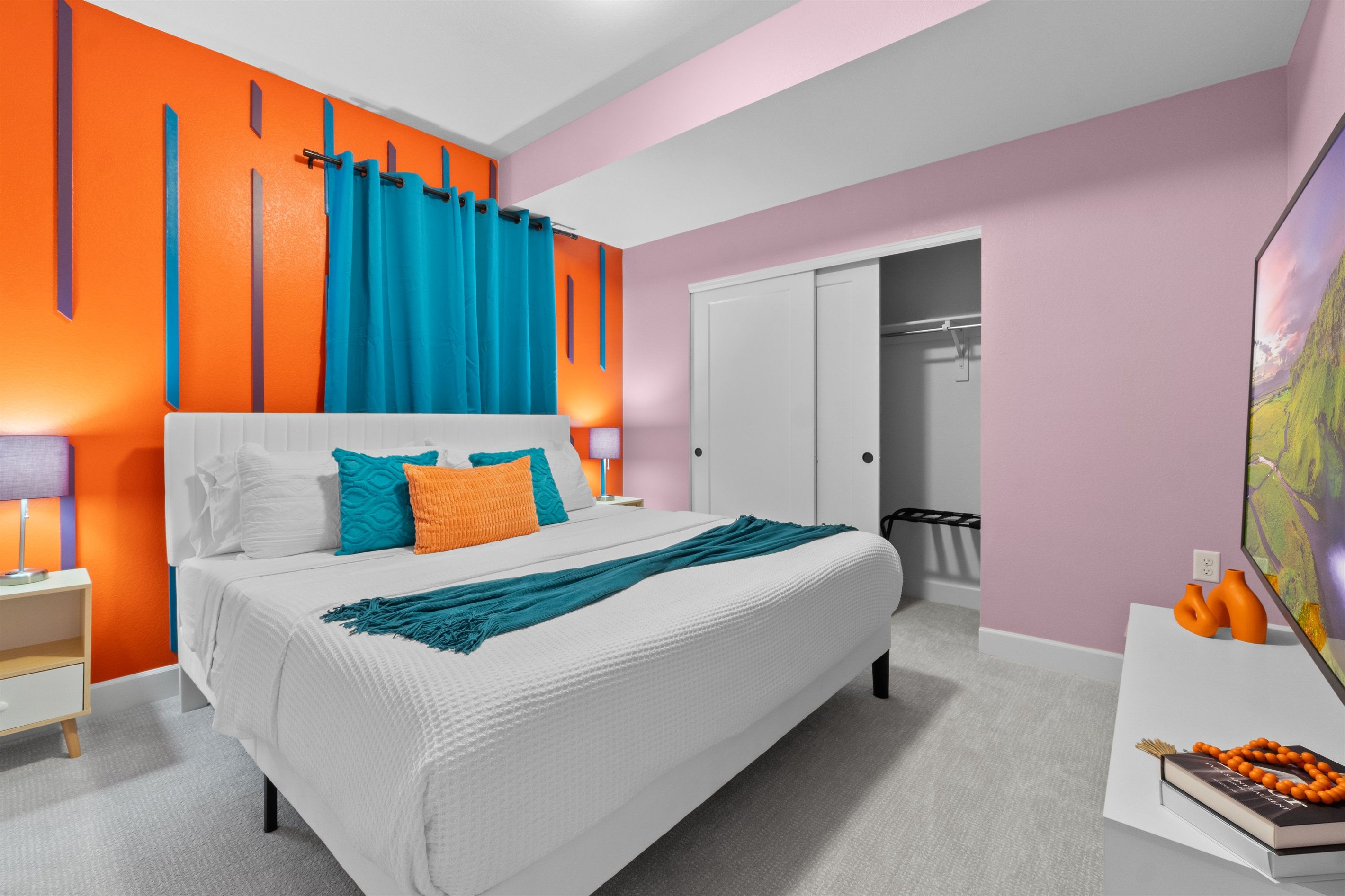 A modern bedroom with a white bed, orange and blue accent walls, a white wardrobe, and a painting on the wall.