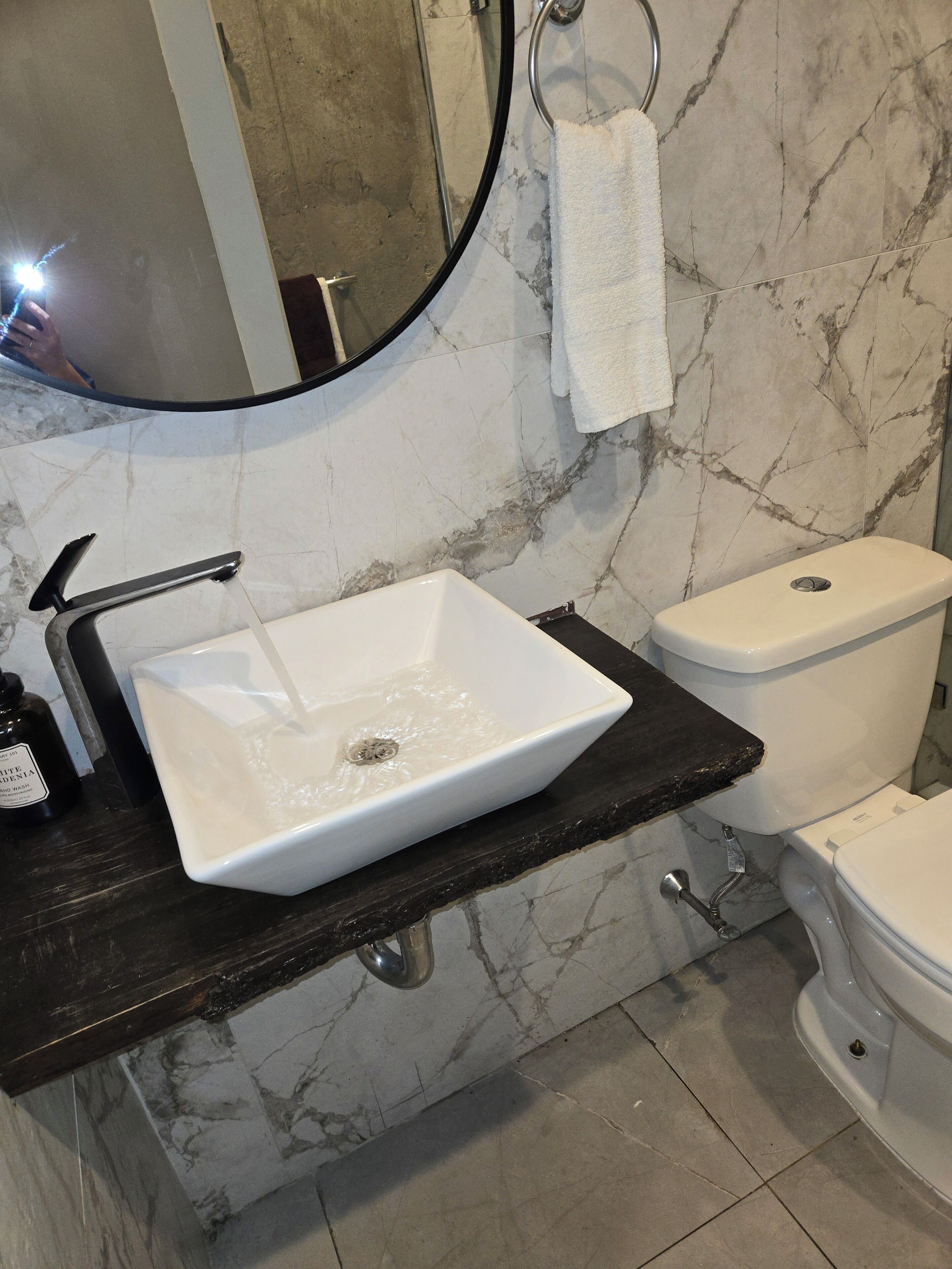 Une salle de bain avec un lavabo blanc, un plan de toilette noir et des toilettes.