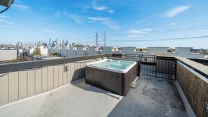 A rooftop patio with a hot tub, a city skyline view, and a concrete floor. - Emerald Luxury Home with Jacuzzi on Private Roof (Philadelphia)