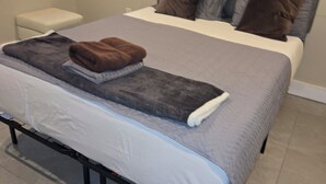 A neatly made bed with a grey and white duvet, a brown throw blanket, and a white pillow. There is a small bedside table with a white lamp. The room has a grey headboard and a decorative wall piece above the bed. - Emerald Luxury Home with Jacuzzi on Private Roof (Philadelphia)