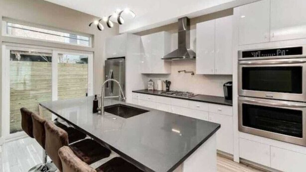 A modern kitchen with white cabinets, a black countertop, and stainless steel appliances including a double oven. - Emerald Luxury Home with Jacuzzi on Private Roof (Philadelphia)