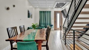 A dining area with a wooden table and green upholstered chairs, a potted plant, and a staircase with a metal railing. - Emerald Luxury Home with Jacuzzi on Private Roof (Philadelphia)