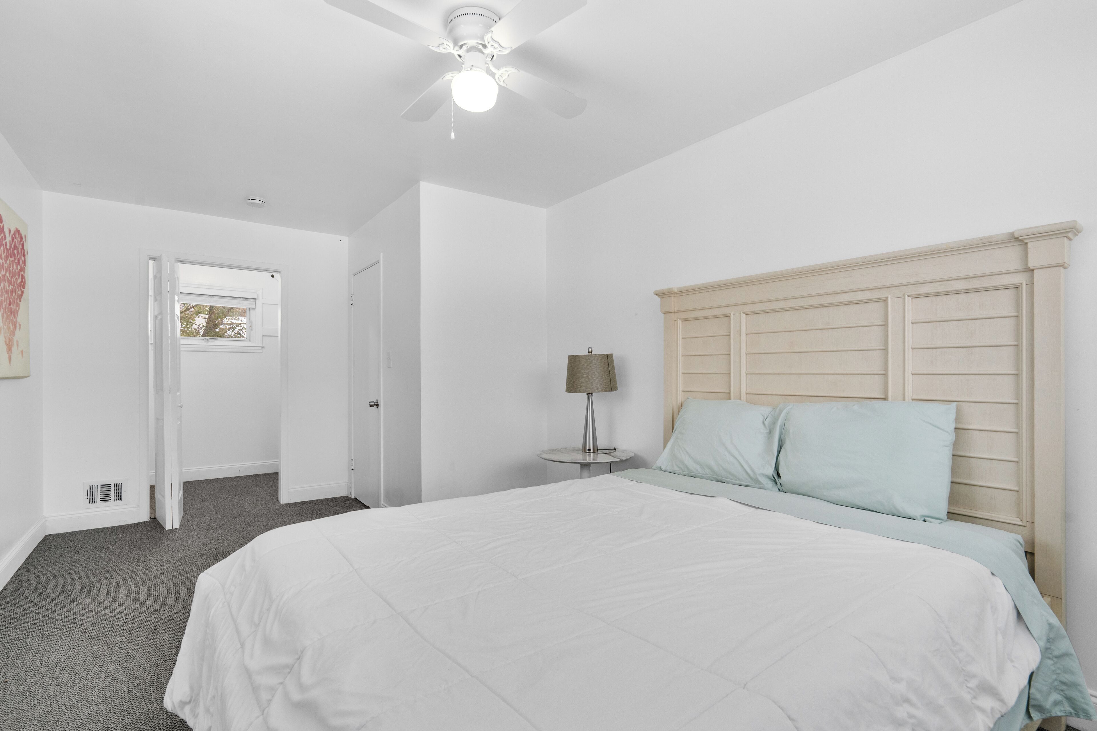 A bedroom with a large bed, a ceiling fan, and a bedside table with a lamp.