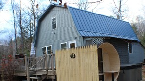 Une maison avec un toit en métal bleu, une terrasse en bois et une clôture en bois comportant une découpe circulaire.