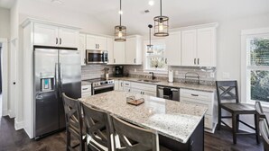 Una cocina moderna con armarios blancos, electrodomésticos de acero inoxidable, encimeras de granito e iluminación colgante.