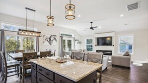 Una cocina amplia con una isla grande, luces colgantes y un comedor con sillas de madera.