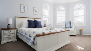 Un dormitorio con cama, una silla, una mesita de noche y una ventana con contraventanas.