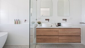 Un baño moderno con tocador blanco, dos lavamanos, armarios de madera y cabina de ducha con mampara de vidrio.