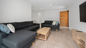 A modern living room with two dark sofas, a wooden coffee table, and a wooden cabinet. - Moonee Beach Getaway - (Moonee Beach)