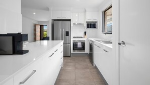 A modern kitchen with white cabinetry, stainless steel appliances, and a large island. - Moonee Beach Getaway - (Moonee Beach)