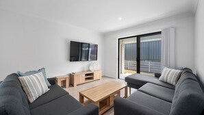 A modern living room with grey sofas, a wooden coffee table, and a TV mounted on the wall. - Moonee Beach Getaway - (Moonee Beach)
