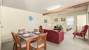A dining area with a wooden table and chairs, a red sofa, and a television in the background. - Myee Court - 500 meters to Urunga Sea Lido (Urunga)