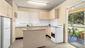 A compact kitchen with a central island, a built-in oven, and a stove. There is a window with blinds, a sink, and a refrigerator. - Myee Court - 500 meters to Urunga Sea Lido (Urunga)