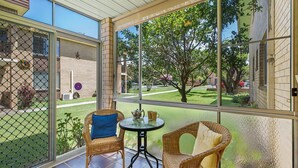 A covered patio with wicker furniture and a table, overlooking a backyard with a brick building and greenery. - Myee Court - 500 meters to Urunga Sea Lido (Urunga)