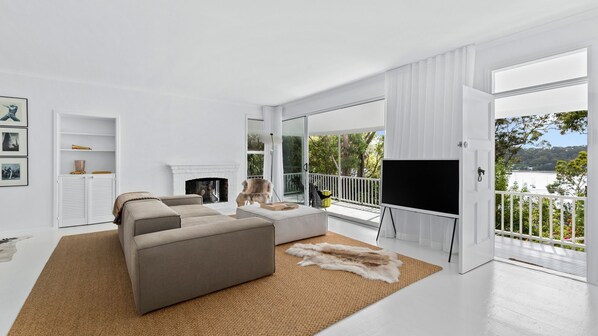 Un salon moderne avec une cheminée, un canapé, un téléviseur et une vue sur un lac, visible à travers de grandes fenêtres.
