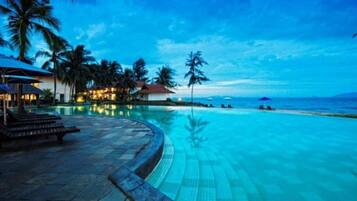 A resort pool with a curved edge, palm trees, and a beach in the background.