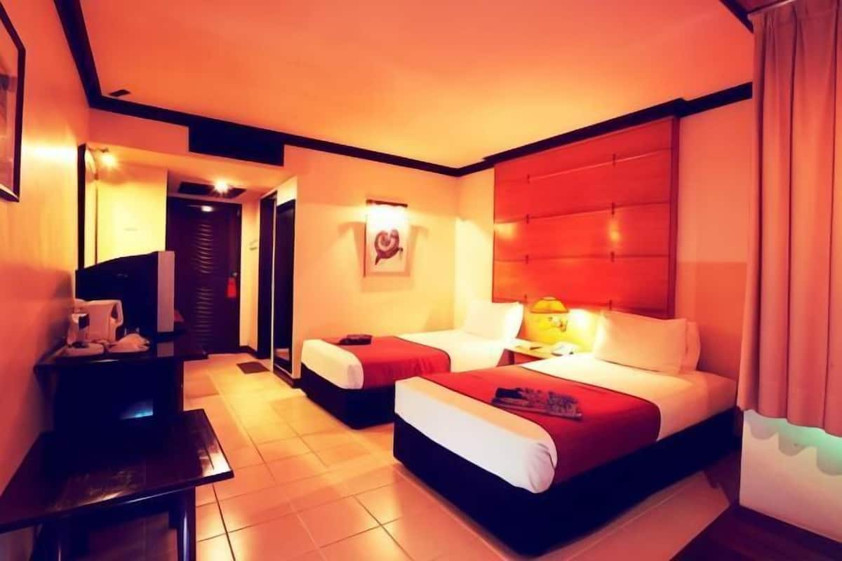 A hotel room with two beds, a desk, a chair, a lamp, and a framed picture on the wall.