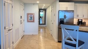 Una cocina con armarios blancos, un refrigerador de acero inoxidable y piso de baldosas.