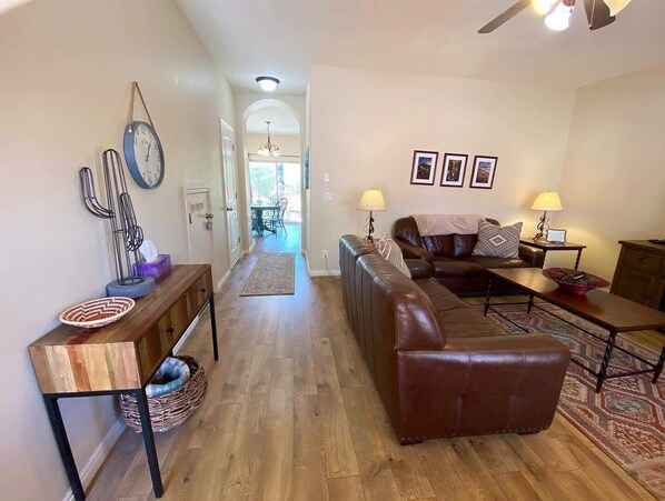 A living room with a leather sofa, a coffee table, and a dining area with a table and chairs. There is a hallway leading to a kitchen area. - Pool & Hot Tub! Close to Zion National Park and Bryce Canyon and hiking trails in Kanab, Utah! (Kanab)