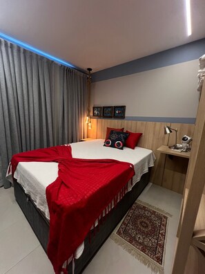 A bedroom with a bed, a nightstand, a lamp, and a wall-mounted shelf.