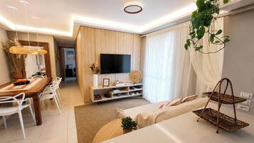 Una sala de estar moderna con un sofá, una mesa de comedor, sillas, un televisor y una planta.
