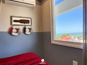 A room with a bed, a window with a view of the sea, and two life rings on the wall. - Casa Refugio Vista Mar - Nautilus Penha (Penha)