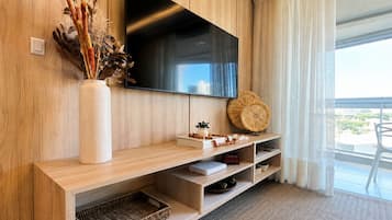Un salon moderne avec un téléviseur à écran plat fixé à un mur en bois, un vase blanc contenant des plantes séchées, un panier en osier et une petite table agrémentée d’objets décoratifs.