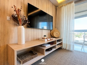 A modern living room with a flat-screen TV mounted on a wooden wall, a white vase with dried plants, a woven basket, and a small table with decorative items. - Casa Refugio Vista Mar - Nautilus Penha (Penha)