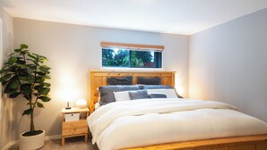 Un dormitorio con una cama, una mesita de noche, una planta en maceta y una ventana con vistas al verdor.
