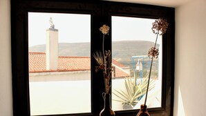 A window with two vases containing dried flowers, overlooking a building with a tiled roof and a statue on a pedestal.