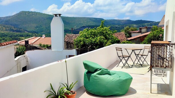 A terrace with a green bean bag, two potted plants, and a view of a hill and buildings.