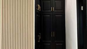 Un couloir doté de deux portes doubles noires, de lambris verticaux de couleur beige et de deux lampes suspendues.