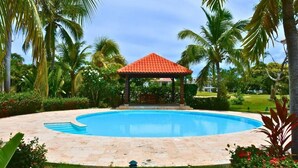 Une piscine agrémentée d’un kiosque, entourée de palmiers et bordée d’une pelouse bien entretenue.