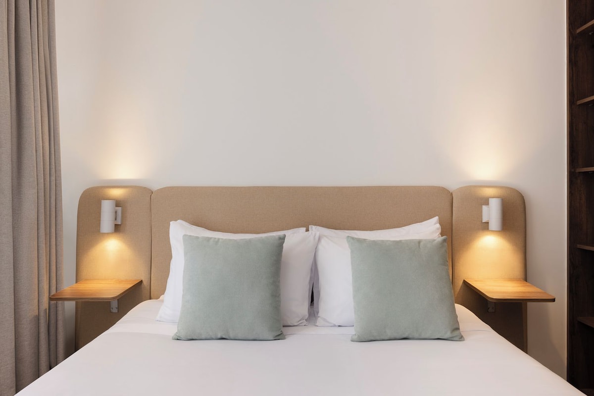 A bed with two pillows, two bedside tables, and two wall-mounted lamps.